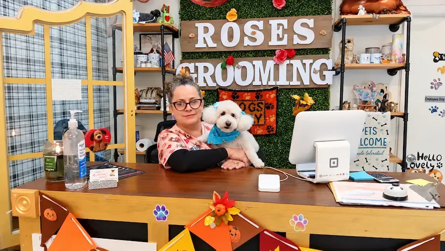 Groomer with a freshly groomed white dog at the Rose’s Grooming House front desk in Miami Springs